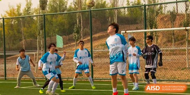 Students wearing jerseys and playing soccer or a similar field sport outdoors at Shanxi Plinth International School.