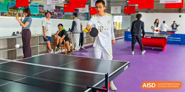 Student playing table tennis (ping pong) indoors, wearing a school jersey, at Shanxi Plinth International School.