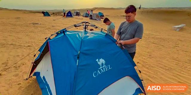 A student assembling a blue Camel brand tent in the desert during an outdoor education trip for Shanxi Plinth International School.