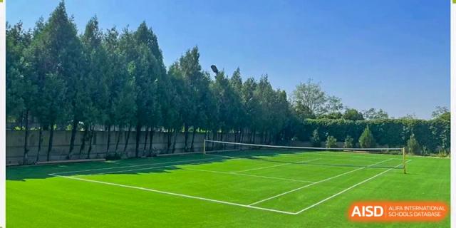 An empty, well-maintained tennis court with green artificial turf, likely located at the facilities of Shanxi Plinth International School.