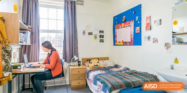 Bright student dormitory room with a single bed, bedside table, and decorations on the wall at Shanxi Plinth International School.