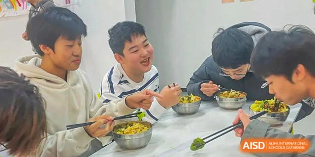 Students happily eating a meal together out of metal bowls in the dining area or cafeteria at Shanxi Plinth International School.