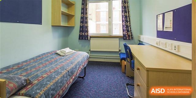 A simple, neat student dormitory room with a single bed, small desk, and window at Shanxi Plinth International School.