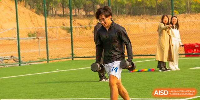A male student smiles while running and holding dumbbells on the athletic field at Shanxi Plinth International School.