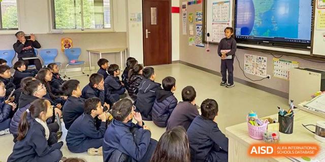 Students sitting on the floor facing the front of a classroom at Wuxi Boston International School.