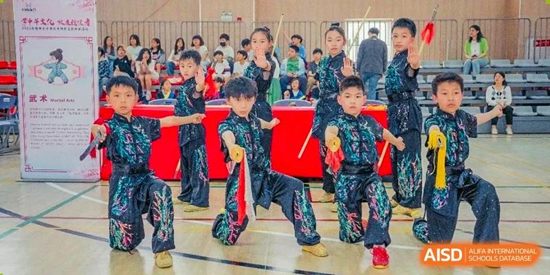 Students in black and green traditional outfits performing with sticks at Wuxi Boston International School.