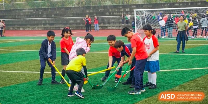 Children playing a sport similar to field hockey on a grassy pitch at Wuxi Boston International School.