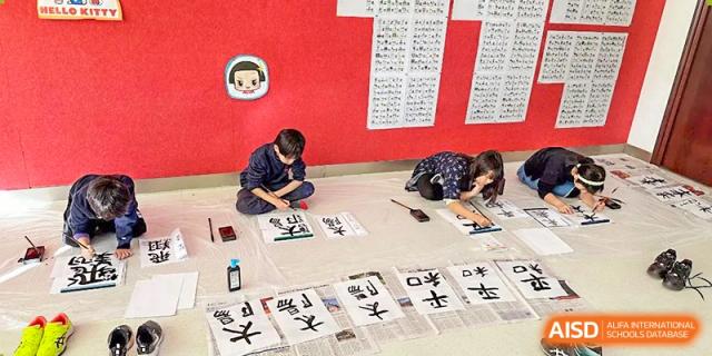 Students practicing calligraphy on large paper on the floor at Wuxi Boston International School.