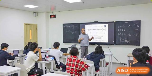 A male teacher explains a concept written on a blackboard to students in a classroom at Wuhan Britain-China School.