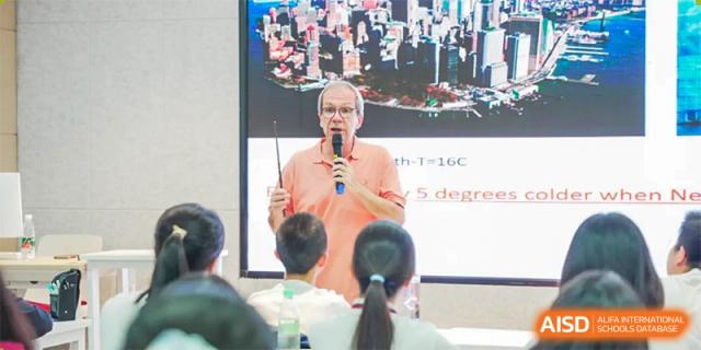A speaker in a peach-colored shirt holds a microphone while presenting to a large audience of students at Wuhan Britain-China School.