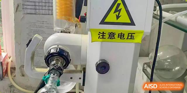 A close-up of industrial or laboratory equipment with a yellow warning sign that reads "注意 电压" (Caution Voltage) at Wuhan Britain-China School.