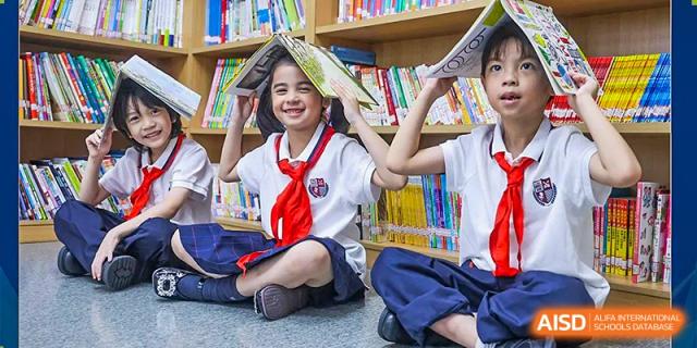 Two elementary-age students in white shirts and red scarves smile while holding books, representing reading and learning at Wuhan Britain-China School.