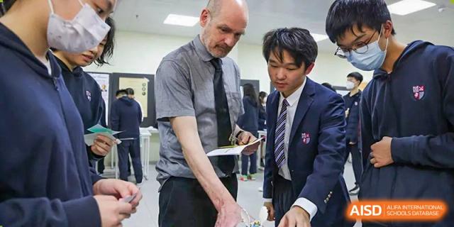 A student in a tie interacts with a teacher or staff member, likely in a school event or activity at Wuhan Britain-China School.