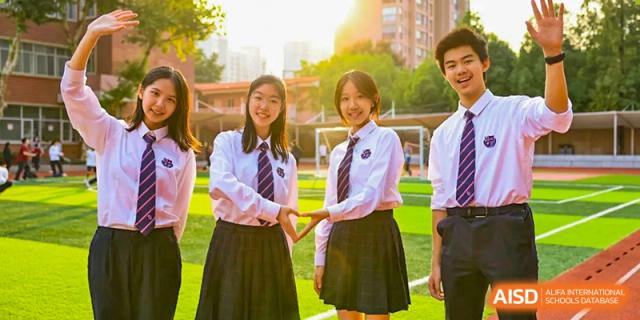Two female students in matching uniforms stand outdoors on the campus of Wuhan Britain-China School.