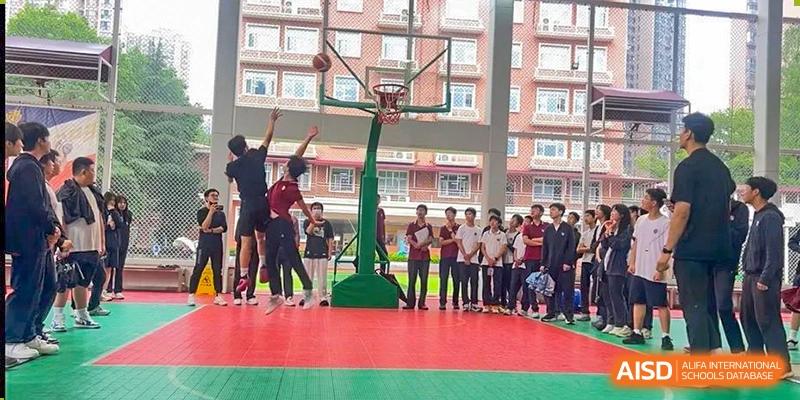 Students from Wuhan Britain-China School gather to watch a basketball drill or game on an outdoor court.