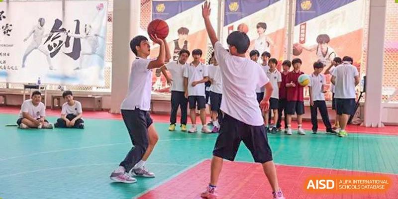 Two students from Wuhan Britain-China School practicing a basketball shot while classmates observe in the background.