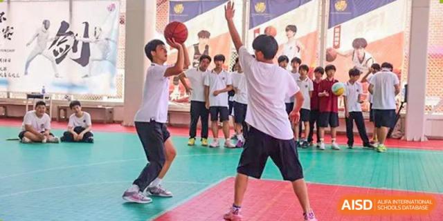 Two students from Wuhan Britain-China School practicing a basketball shot while classmates observe in the background.