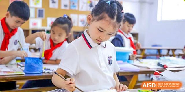 A female student from Wuhan Britain-China School in uniform is focused on writing or drawing in a notebook.