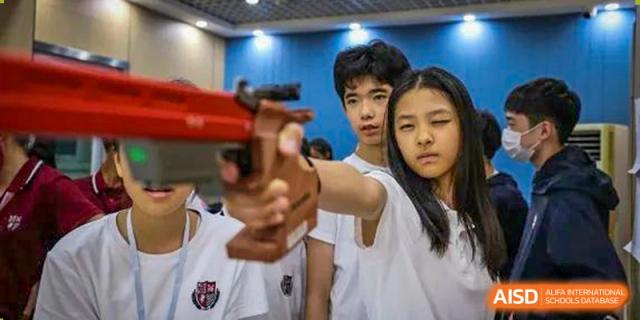 Two students from Wuhan Britain-China School aiming with a slingshot or similar device during an extracurricular activity.