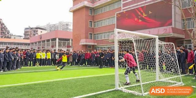 A group of students from Wuhan Britain-China School gathered around a goalpost on the soccer field during a training session or game.
