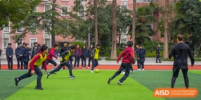 Students from Wuhan Britain-China School playing soccer on a grassy field in the school courtyard.