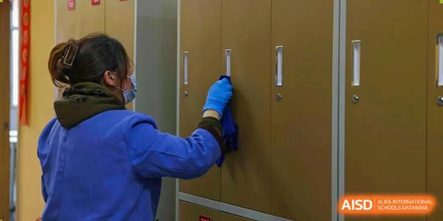 A person wearing a blue glove cleans a row of tan lockers, part of the facilities at Wuhan Britain-China School.