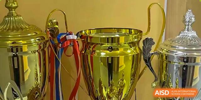 A close-up shot of a large, shiny gold trophy tied with red, white, and blue ribbons, symbolizing an award or competition victory for Wuhan Britain-China School.