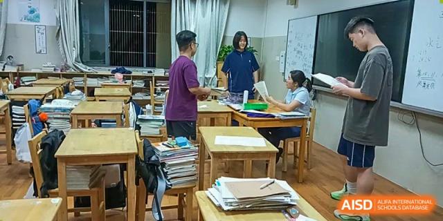 A teacher helping a group of students gathered around a desk with stacked papers and materials for a school project, at Ningxiang Country Garden School.
