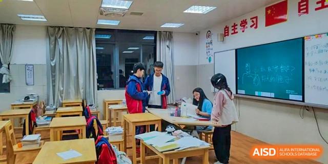 Students in uniform working together on an assignment or collaborative group task in a well-lit classroom setting, at Ningxiang Country Garden School.