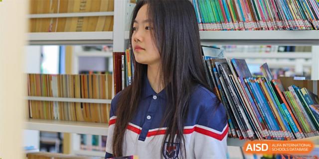 A portrait of a female student wearing the school uniform (blue, red, and white polo shirt) standing in the library, at Ningxiang Country Garden School.