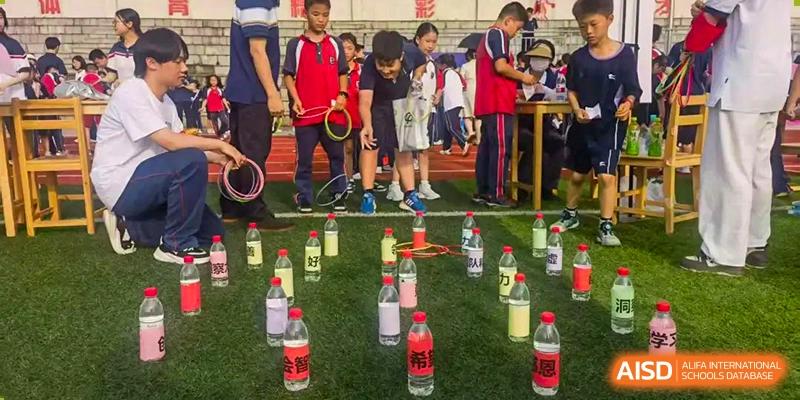 A group of students outdoors participating in a school game, looking down at rows of numbered plastic bottles with red labels on grass, at Ningxiang Country Garden School.