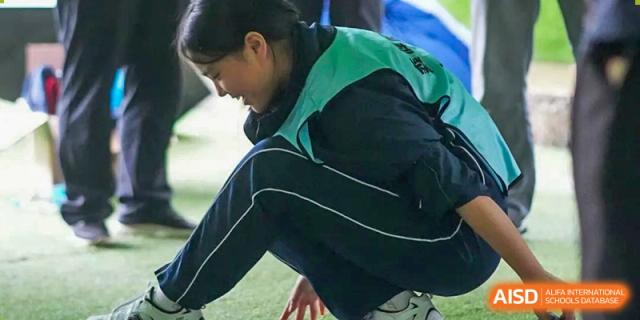 A female student in a dark blue and teal tracksuit kneeling or crouching on a sports field during an activity, at Ningxiang Country Garden School.