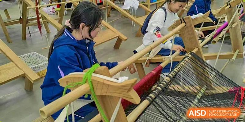 A student working on a traditional wooden loom or weaving device, creating a textile with green and red thread, at Ningxiang Country Garden School.