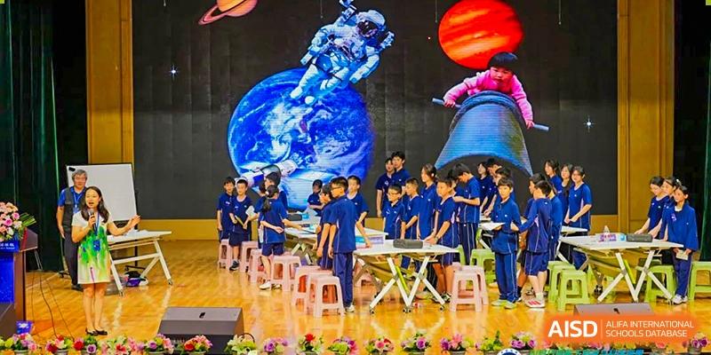 A group of students in blue uniforms standing together on a stage with a brightly lit backdrop featuring a globe or earth graphic, possibly after a performance, at Ningxiang Country Garden School.