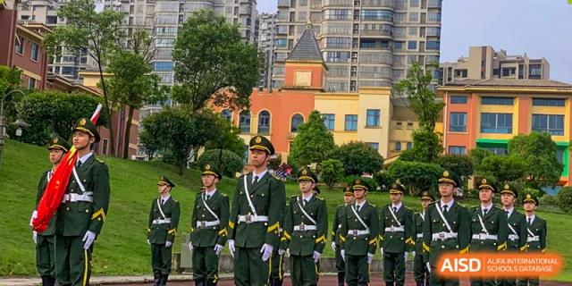 Students dressed in formal green military-style uniforms standing in formation outdoors in front of a colorful school building, at Ningxiang Country Garden School.
