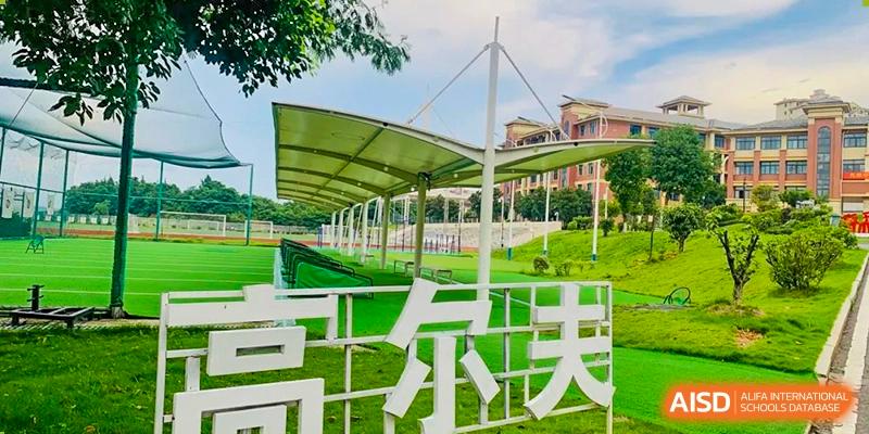 A landscaped area with a large outdoor sign or sculpture with Chinese characters, near modern school buildings and a sheltered outdoor space, at Ningxiang Country Garden School.