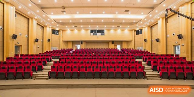 An image of an empty auditorium or theater with rows of bright red seats and a wooden stage, ready for a school event, at Ningxiang Country Garden School.