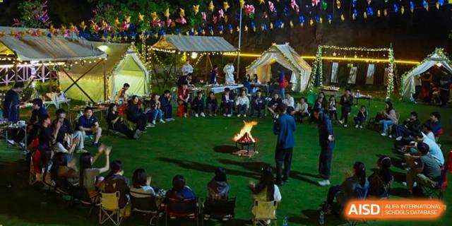 Students and people gathered around a campfire at night on a grassy area during an outdoor school event or camping activity, at Ningxiang Country Garden School.
