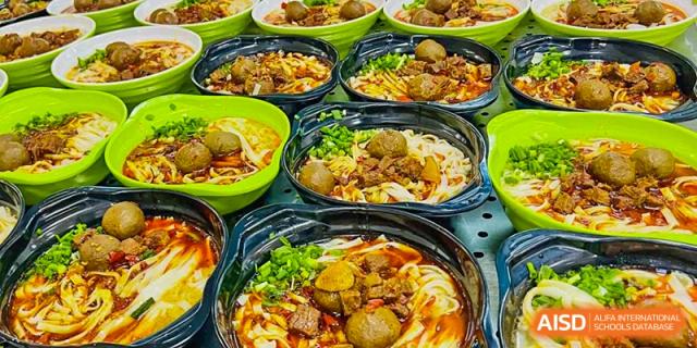 A close-up view of several black bowls containing noodle soup topped with meatballs, sliced beef, and green onions, served as a meal at the canteen of Ningxiang Country Garden School.