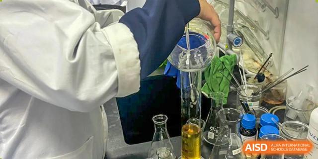 A close-up shot of a student or teacher pouring a liquid from a flask into a beaker as part of a science experiment at Changsha WES (Bilingual) Academy.