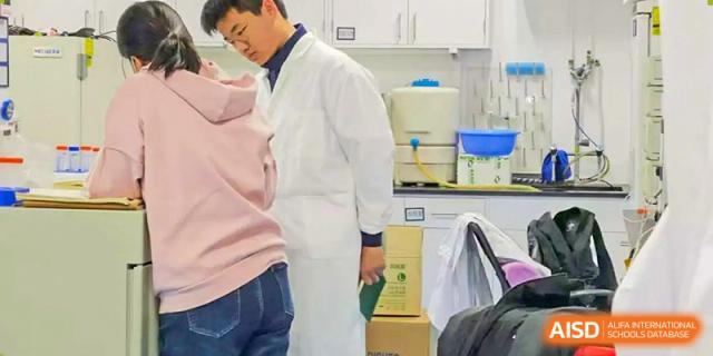A teacher or technician wearing a white lab coat is working with students in a bright, modern science laboratory at Changsha WES (Bilingual) Academy.