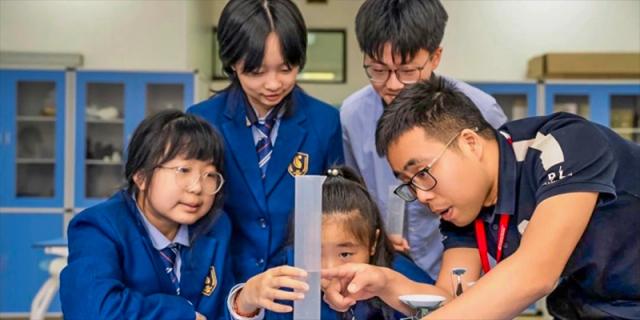 A group of students, including a younger girl, are engaged in a practical math or science exercise, pointing at a measuring tool at Changsha WES (Bilingual) Academy.