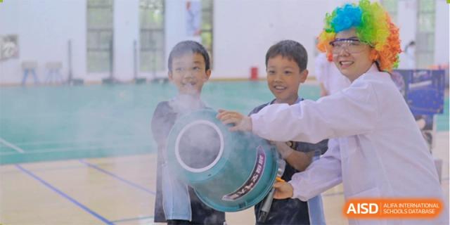 Two young male students watching with excitement as white vapor is released from a large device during an outdoor science demonstration at Changsha WES (Bilingual) Academy.