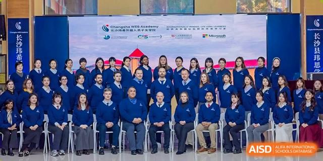 A large group of high school students and faculty posing for a group photograph in front of a banner featuring the school's logo and partners like Microsoft at Changsha WES (Bilingual) Academy.