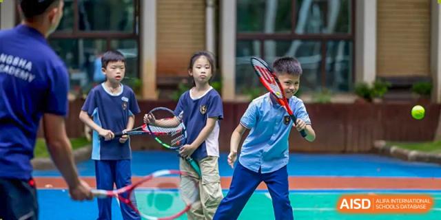 Two young children playing tennis or badminton outdoors, one boy holding a red and black racket with a happy expression at Changsha WES (Bilingual) Academy.