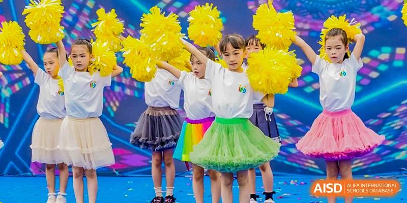 Young children in colorful tutus performing a cheerleading or dance routine with bright yellow pom-poms at Changsha WES (Bilingual) Academy.