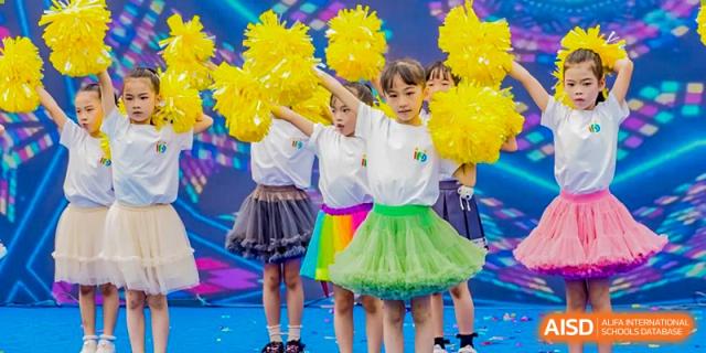 Young children in colorful tutus performing a cheerleading or dance routine with bright yellow pom-poms at Changsha WES (Bilingual) Academy.