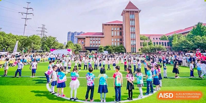 Students and faculty gathered on a lawn for an outdoor event in front of a large brick school building on the campus of Changsha WES (Bilingual) Academy.