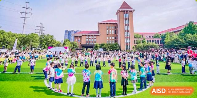Students and faculty gathered on a lawn for an outdoor event in front of a large brick school building on the campus of Changsha WES (Bilingual) Academy.