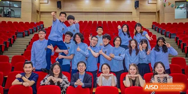 A large group of happy high school students, mostly wearing blue shirts, posing together in a theater or assembly hall at Changsha WES (Bilingual) Academy.